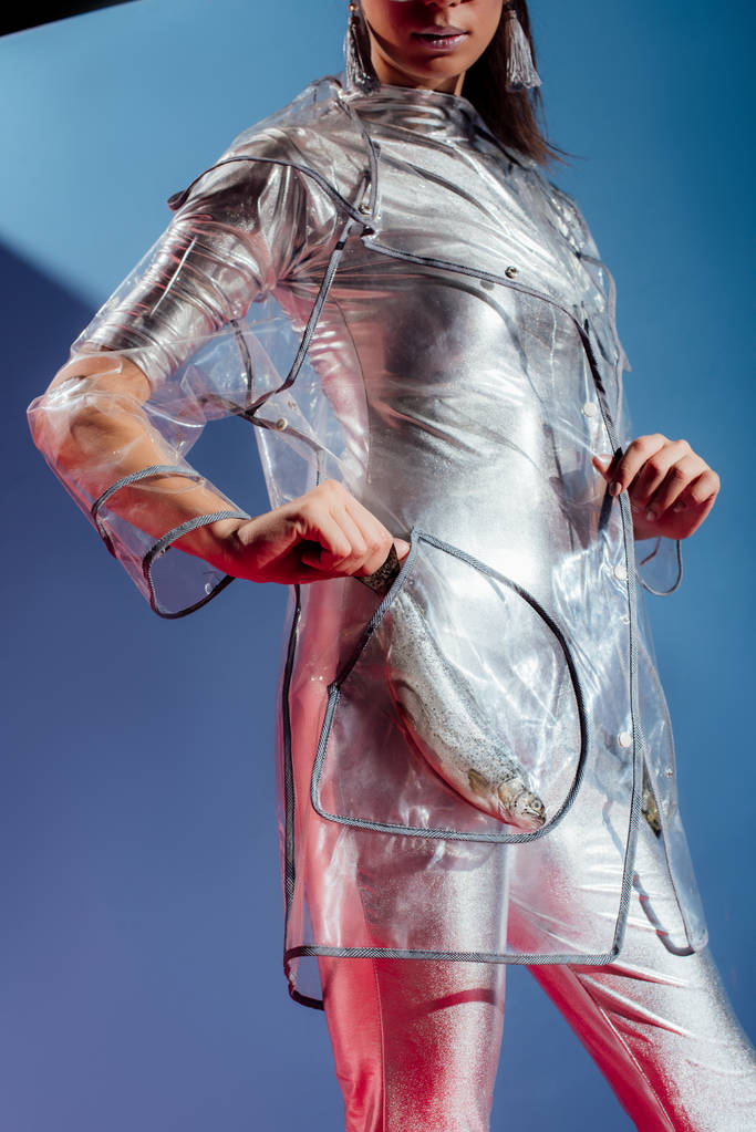 częściowy widok modelu modne w srebrny Body i płaszcz pozowanie z ryb w kieszeni na niebieskim tle - Zdjęcie, obraz