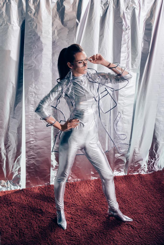 attractive young woman posing in silver bodysuit and raincoat on metallic background - Photo, Image