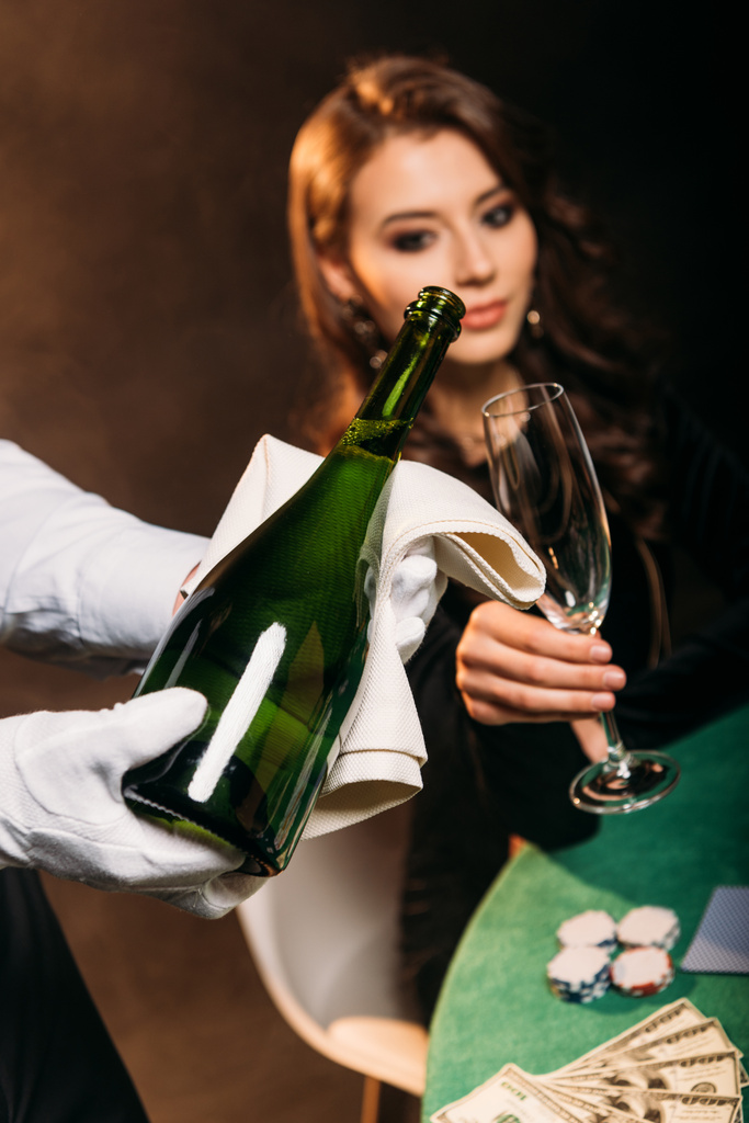 selectieve aandacht van de ober gieten van champagne in glas voor aantrekkelijk meisje op de pokertafel in casino - Foto, afbeelding