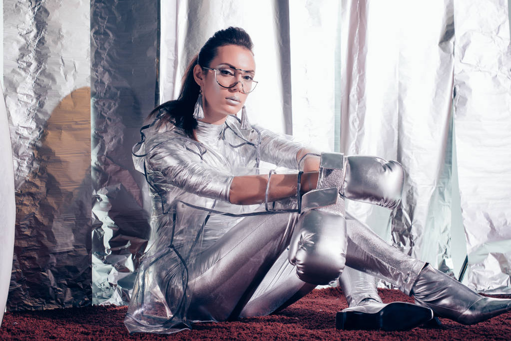 morena joven posando en traje de cuerpo, impermeable y guantes caja de plata sobre fondo metálico
 - Foto, Imagen