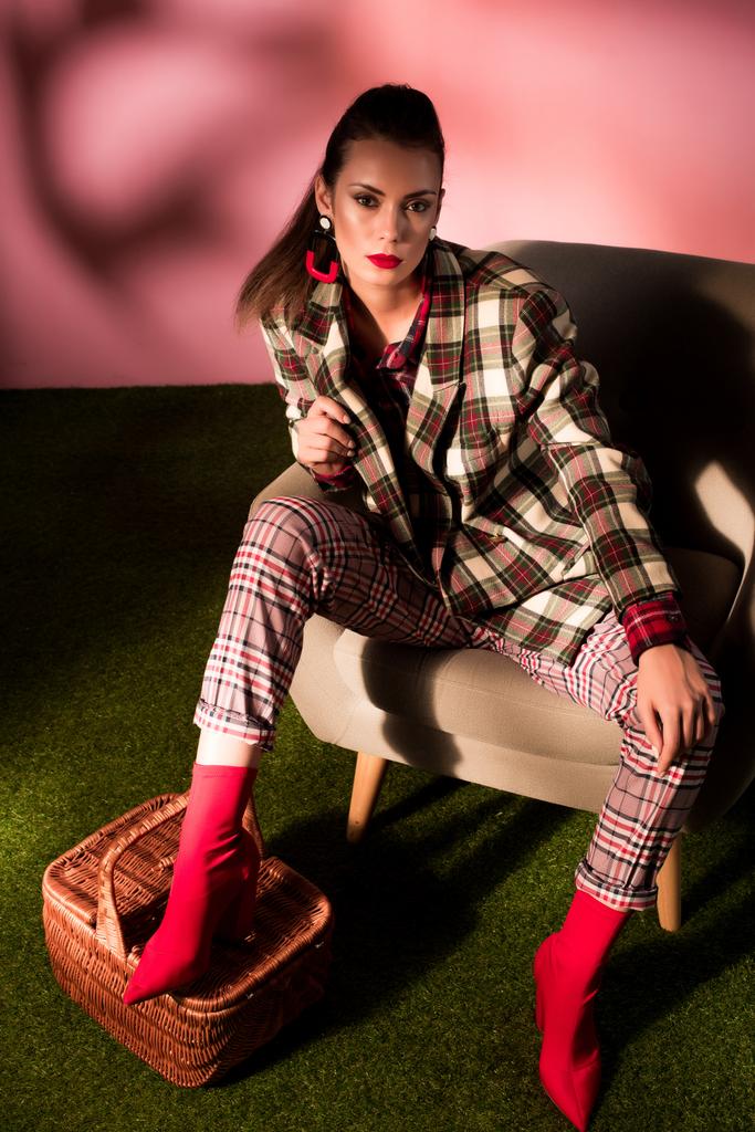 fashionable woman in checkered suit posing in armchair with basket  - Photo, Image
