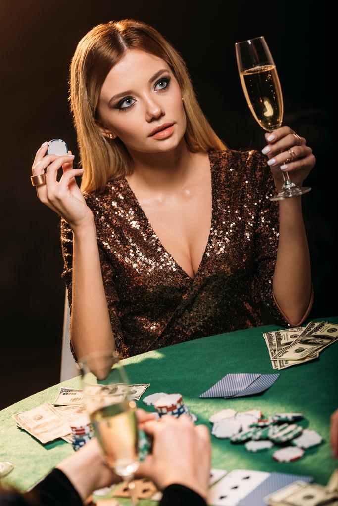 aantrekkelijk meisje bedrijf glas champagne en poker chip aan tafel in casino - Foto, afbeelding