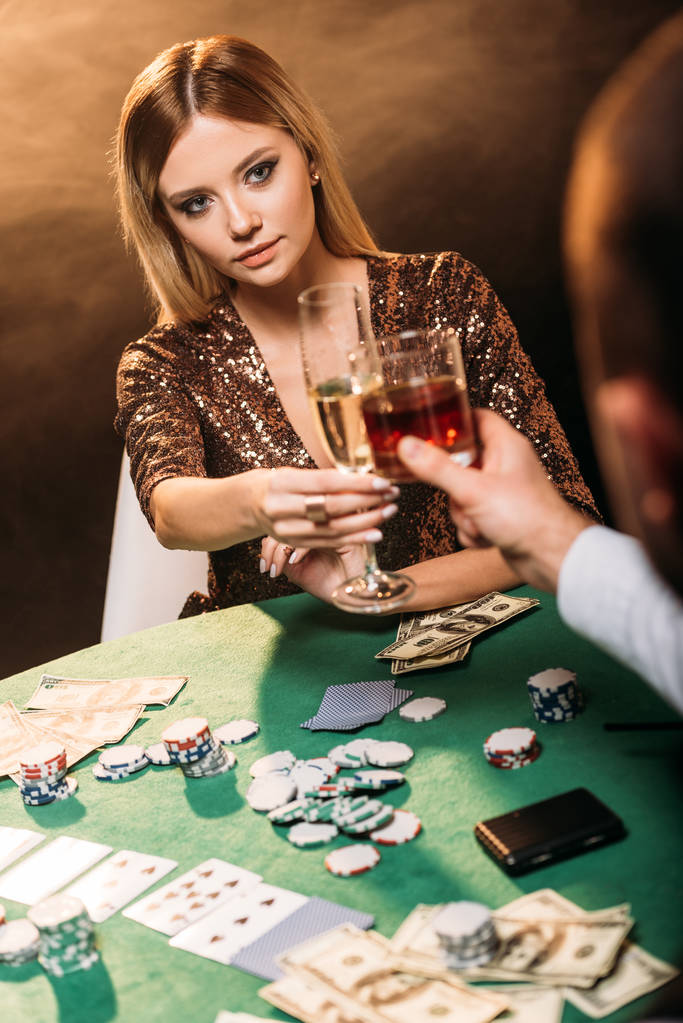 attractive girl and croupier clinking with glasses of alcohol drinks while playing poker at casino - Photo, Image