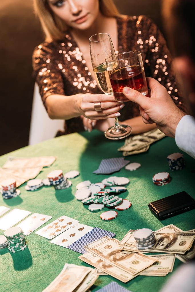 περικομμένη εικόνα κοριτσιού και κρουπιέρης τσούγκριζαν με ποτήρια αλκοόλ ποτά ενώ παίζετε πόκερ στο καζίνο - Φωτογραφία, εικόνα