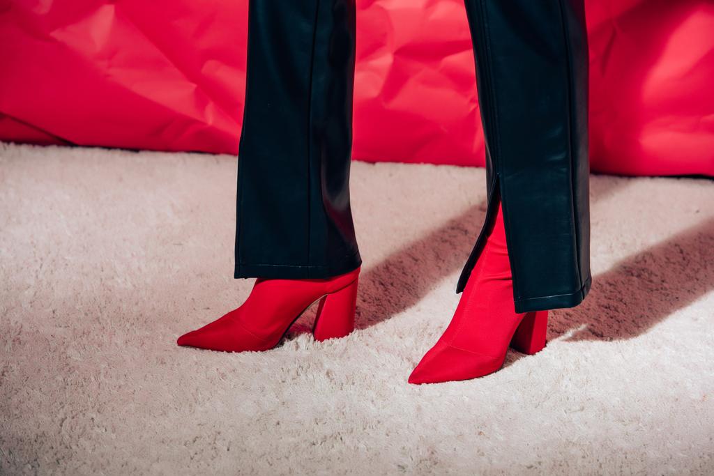 gedeeltelijke weergave van vrouw poseren in rode hoge hakken schoenen en zwart lederen broek   - Foto, afbeelding