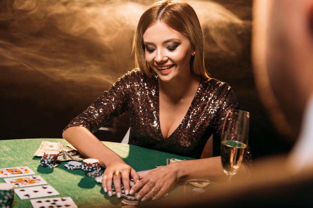 χαμογελώντας όμορφη κοπέλα λαμβάνοντας μάρκες πόκερ και κοιτάζοντας προς τα κάτω στο καζίνο - Φωτογραφία, εικόνα
