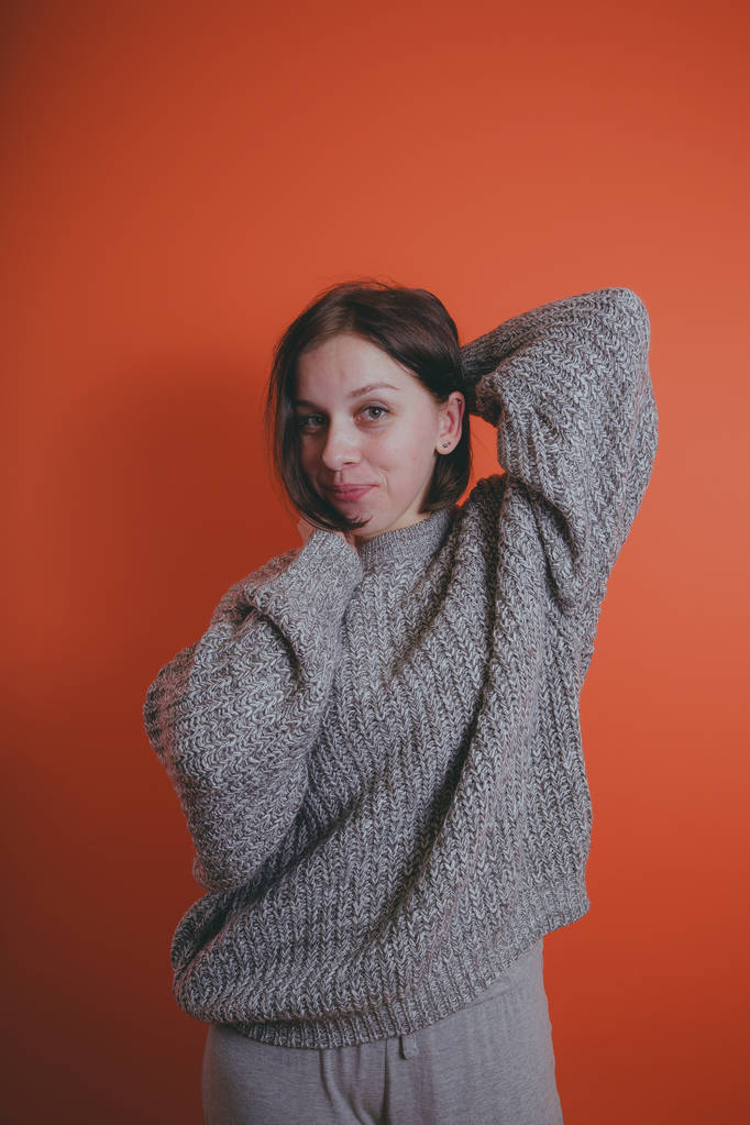 Young girl in warm grey sweater posing on orange background, woman with short haircut in knitted sweater, space for text - Photo, Image