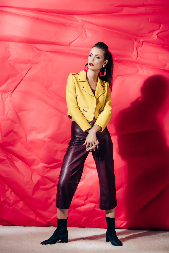 赤の背景に黄色のレザー ジャケット スタイリッシュなブルネット モデルポーズ - 写真・画像