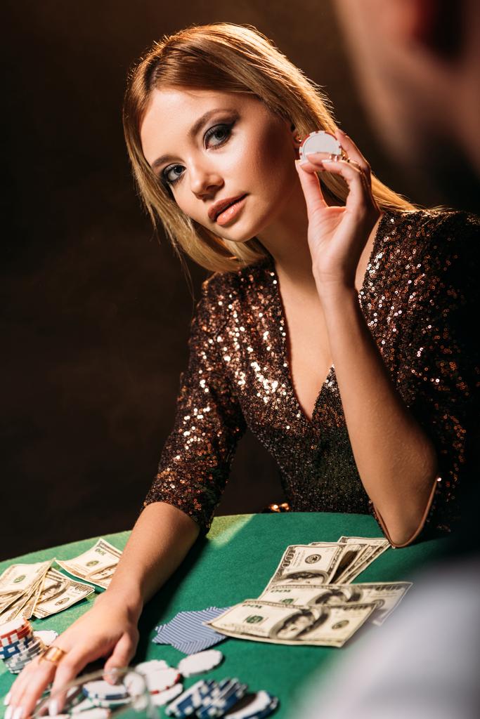 aantrekkelijk meisje pokerfiche houden en kijken naar croupier bij casino - Foto, afbeelding