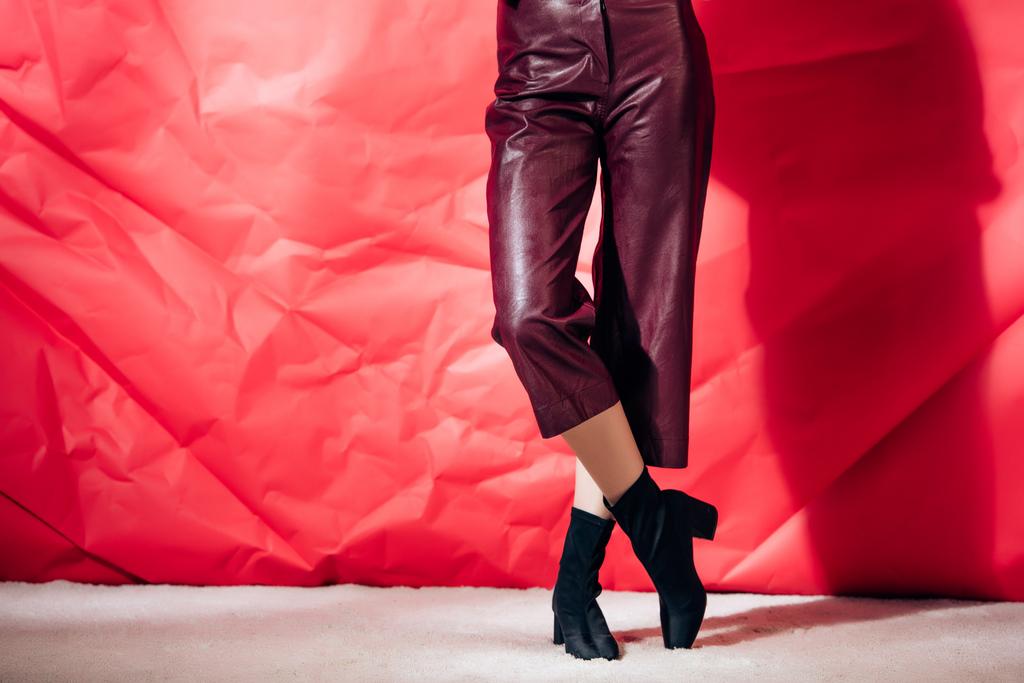 vue en coupe basse du modèle posant en pantalon en cuir bordeaux sur fond rouge
 - Photo, image
