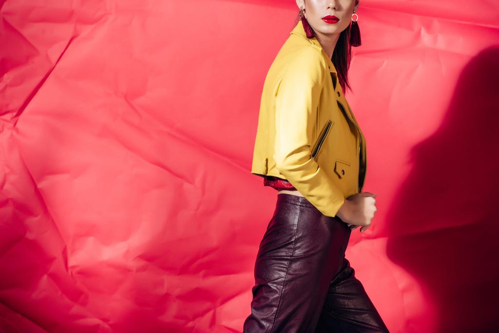 赤の背景に黄色のレザー ジャケットでポーズ ファッショナブルなモデルのビューをトリミング - 写真・画像