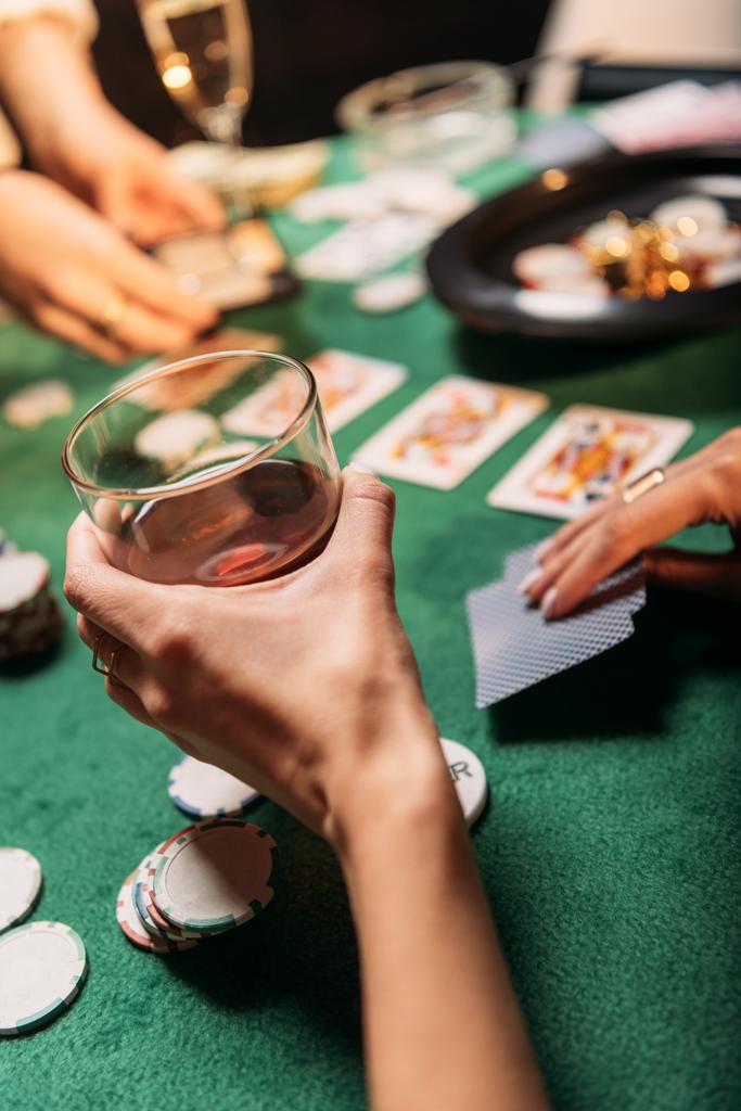 immagine ritagliata di donna che gioca a poker e tiene un bicchiere di whisky a tavola nel casinò
 - Foto, immagini