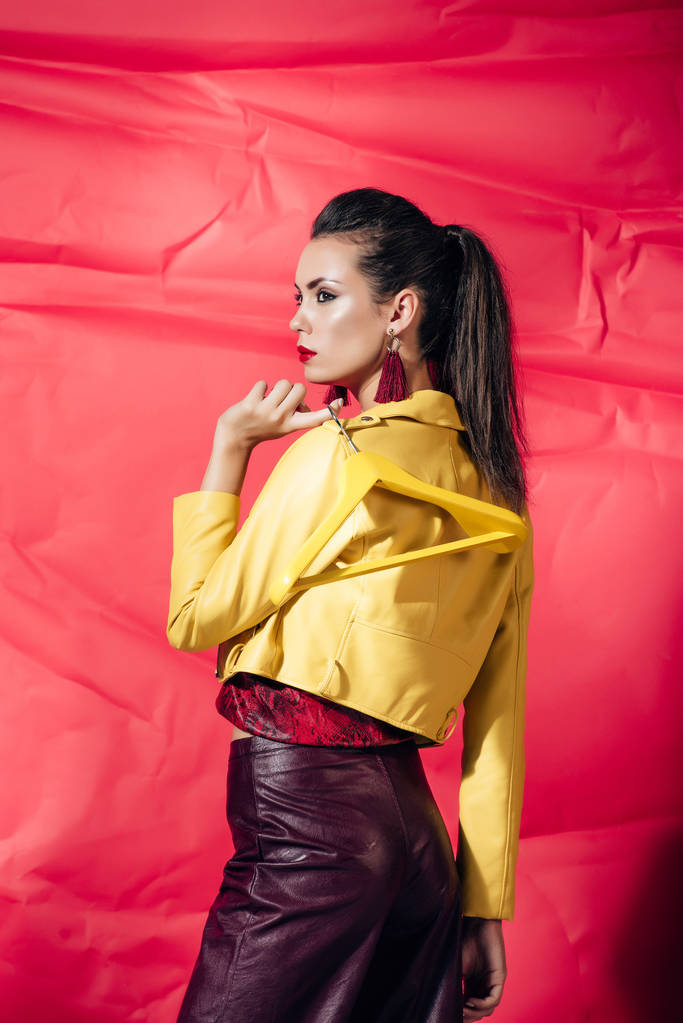 houkutteleva nuori nainen keltainen nahka takki poseeraa ripustin punaisella taustalla
 - Valokuva, kuva