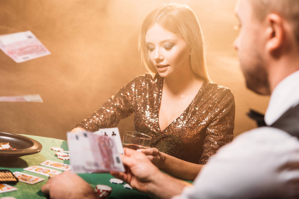 attractive girl playing poker with croupier at casino, money falling on table - Photo, Image