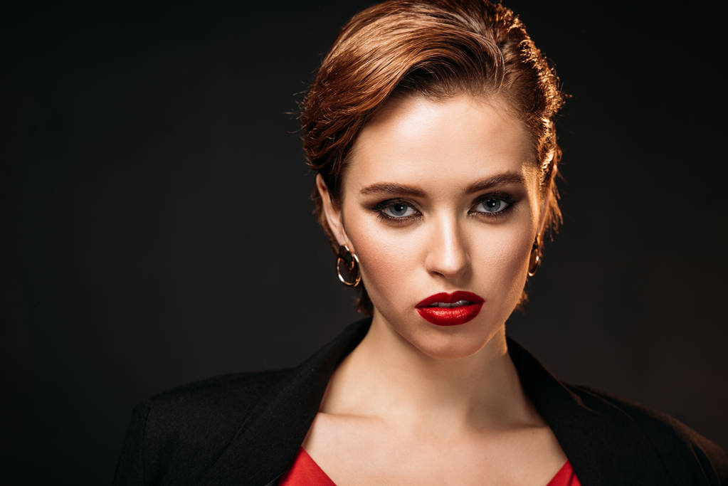portrait of attractive girl in red dress and black jacket looking at camera isolated on black - Photo, Image