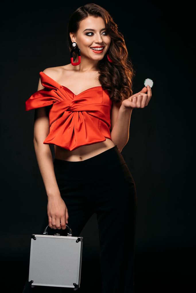 heureux belle fille aux cheveux bruns en corset rouge tenant boîte à argent et jetons de casino isolés sur noir
 - Photo, image