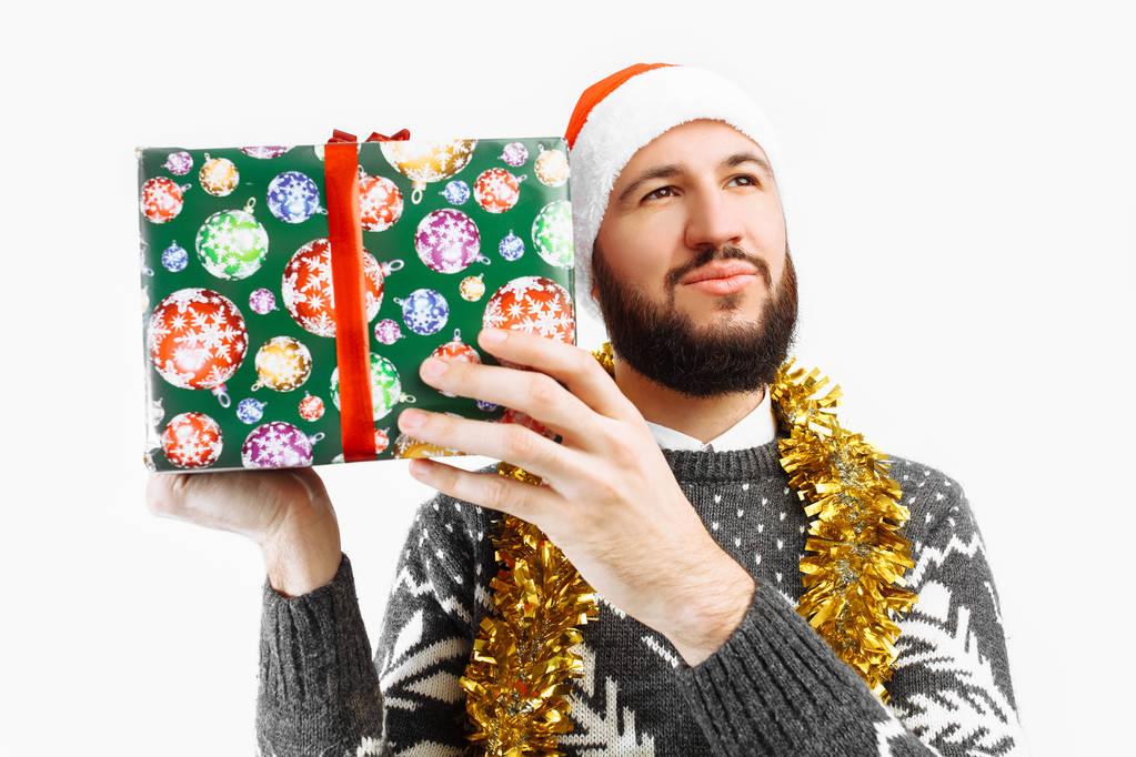 ένας άνθρωπος με ένα χριστουγεννιάτικο δώρο, ψάχνει μέσα, σε λευκό φόντο - Φωτογραφία, εικόνα