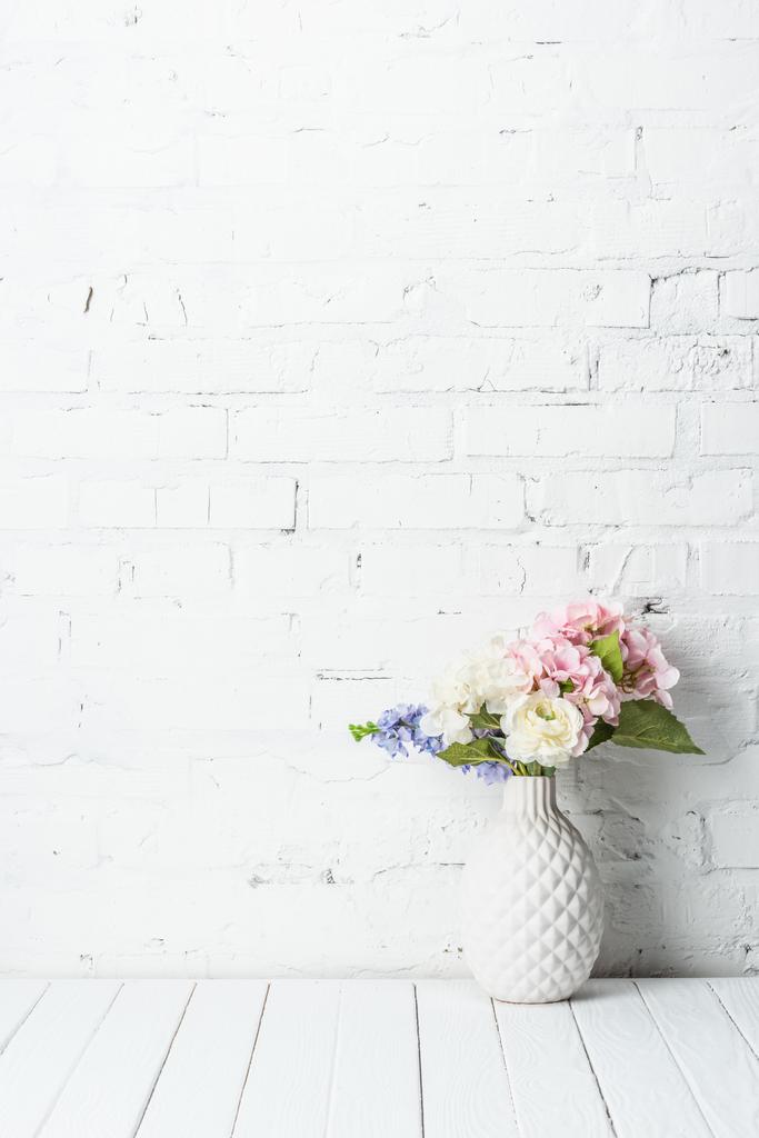 vase en céramique avec bouquet de fleurs sur table rustique en bois près du mur de briques
 - Photo, image