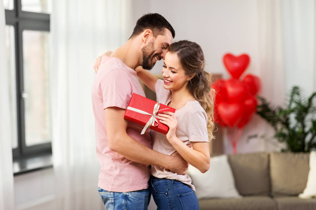 glückliches Paar mit Geschenkbox, das sich zu Hause umarmt - Foto, Bild