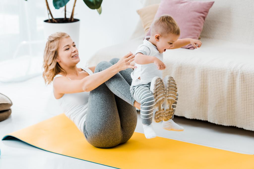 vrouw liggend op fitness mat terwijl bedrijf schattig zoontje - Foto, afbeelding