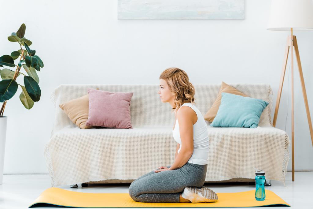 tired woman in sportswear on yellow fitness mat in living room - Photo, Image