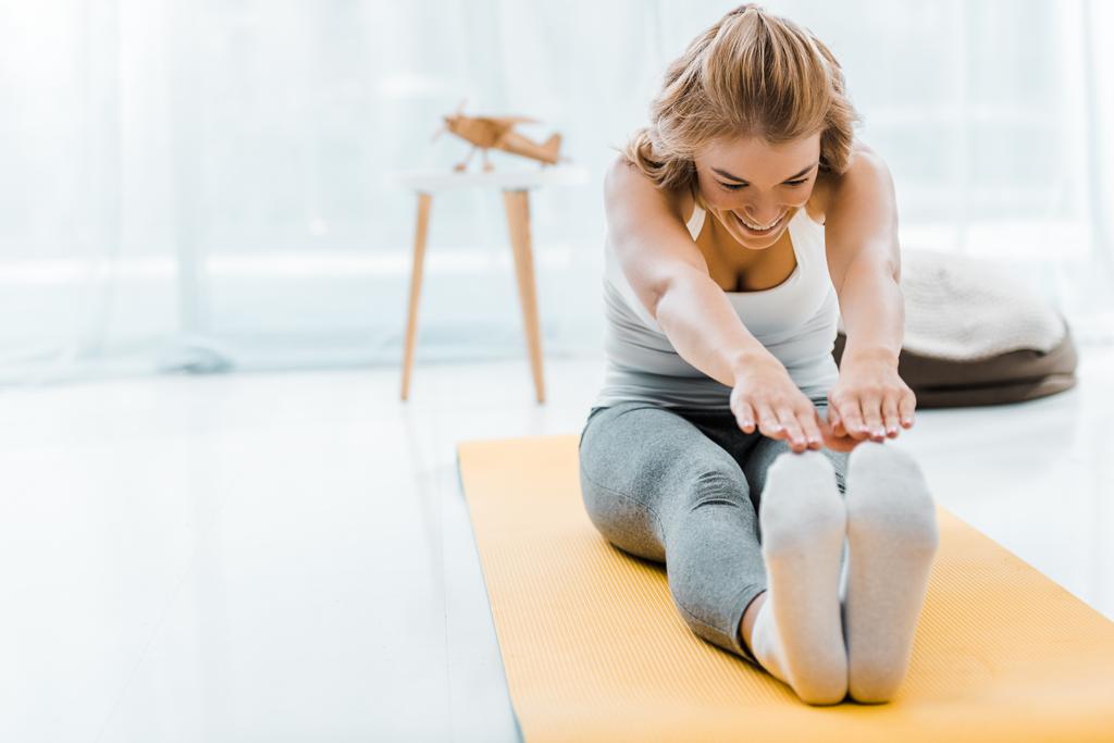 hymyilevä nainen urheiluvaatteet tekee venyttely liikunta kunto matto olohuoneessa
 - Valokuva, kuva