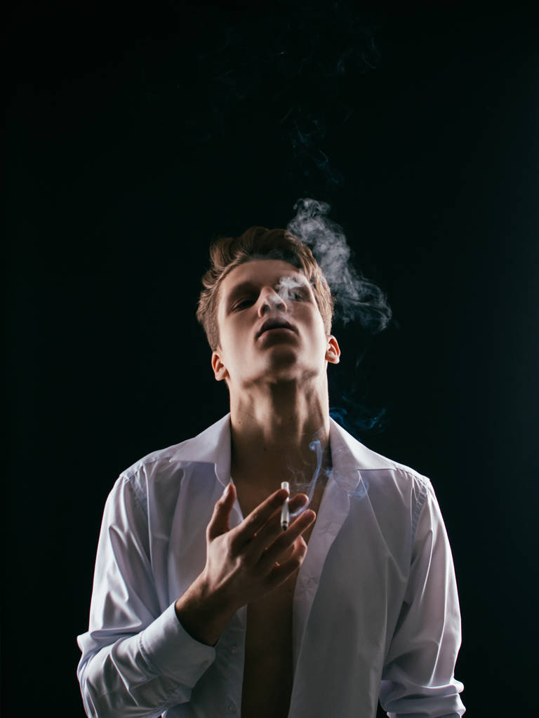 Όμορφος νεαρός άνθρωπος καπνίζει ένα τσιγάρο, studio γυρίσματα. - Φωτογραφία, εικόνα