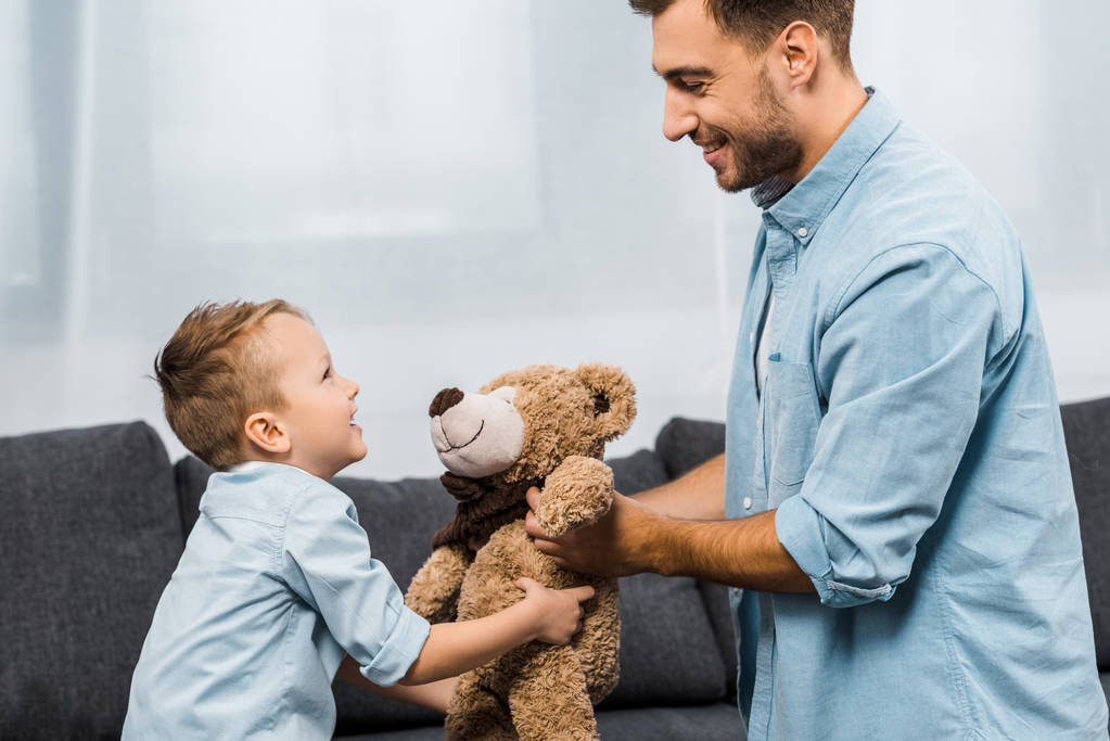 sorrindo pai e filho segurando ursinho de pelúcia na sala de estar
 - Foto, Imagem