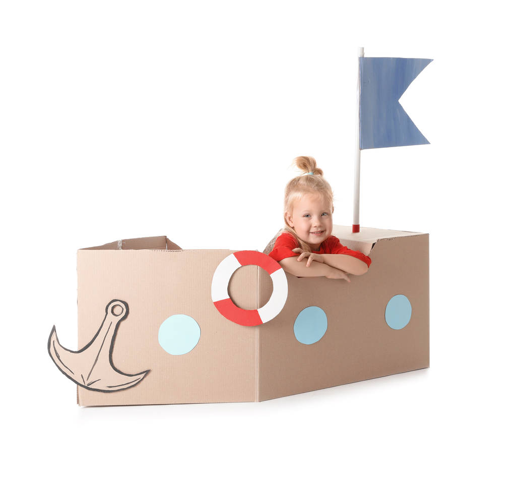 Schattig klein meisje speelt met kartonnen schip op witte achtergrond - Foto, afbeelding