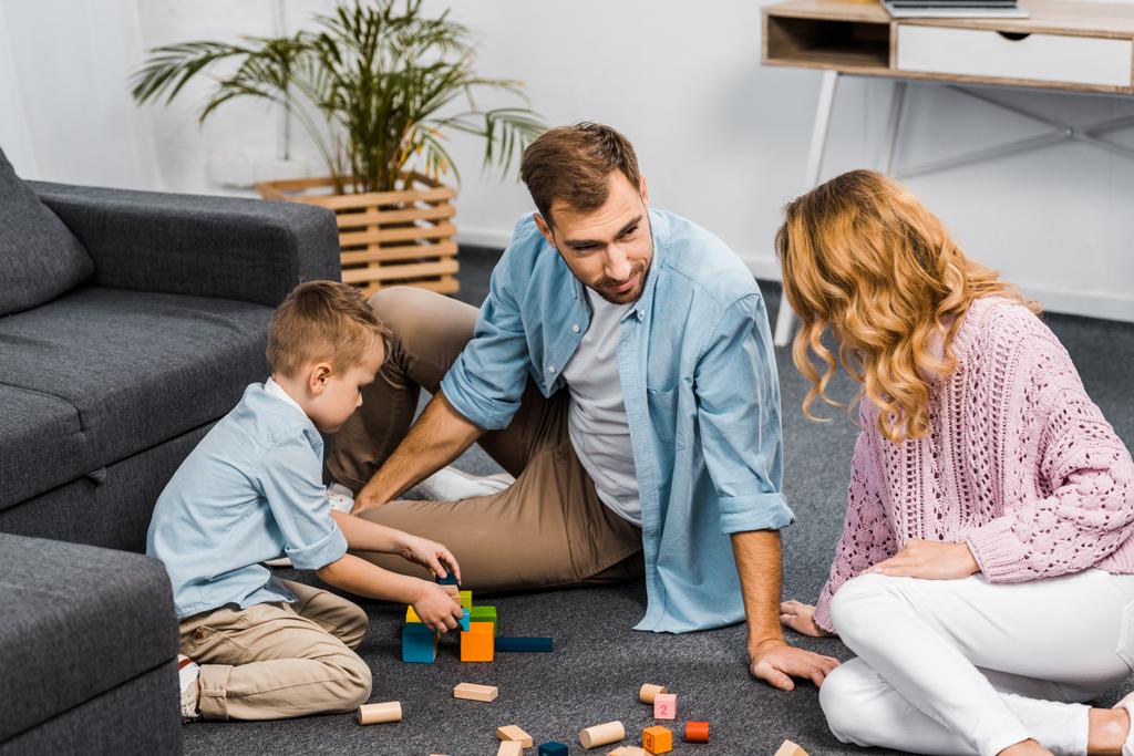 parents and son playing with wooden blocks on floor in living room - Photo, Image