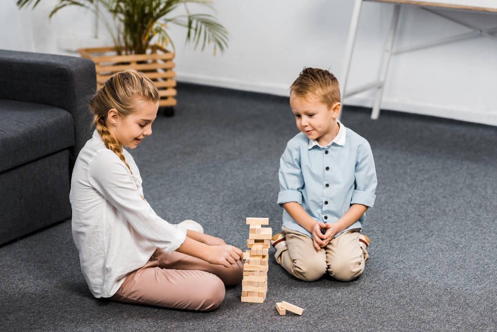 cute siblings sitting on floor and playing blocks wood tower game in living room - Photo, Image