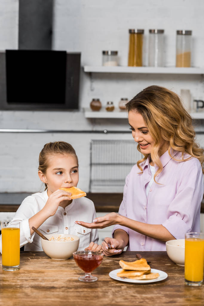 Lächelnde Mutter schaut süße Tochter beim Toast mit Marmelade an - Foto, Bild