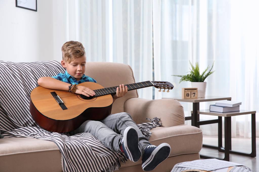 Lindo niño tocando la guitarra en el sofá en la habitación
 - Foto, imagen