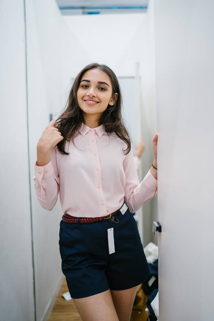 Portrait of a young and beautiful Indian Asian woman trying out new clothing in a fitting room in a fashion shop in a mall. - Photo, Image