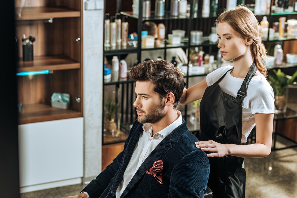 high angle view of hairdresser doing hairstyle to handsome young man in beauty salon - Photo, Image