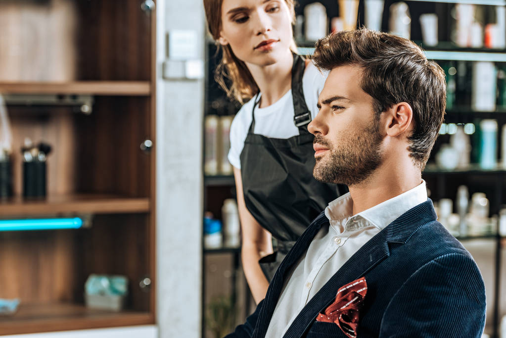 привлекательная женщина-парикмахер смотрит на красивого молодого человека в салоне красоты
 - Фото, изображение