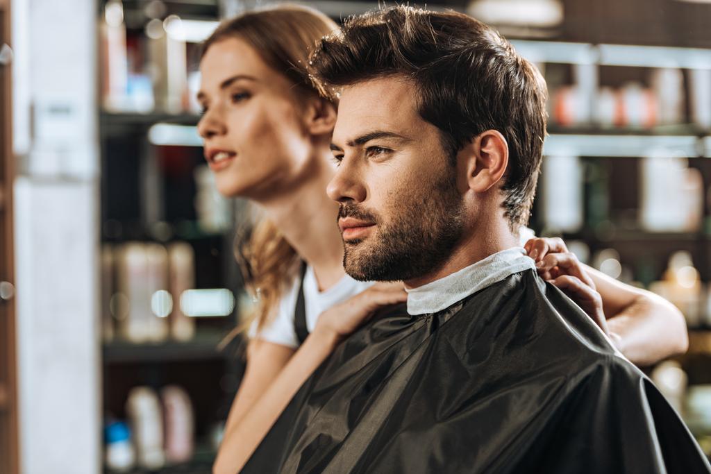handsome young man and beautiful female hairstylist looking away in beauty salon - Photo, Image