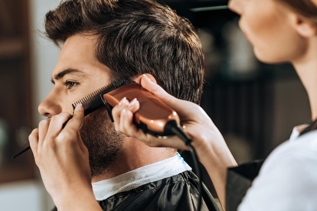 обрезанный снимок парикмахера, держащего расческу и стригущего волосы для красивого клиента
 - Фото, изображение