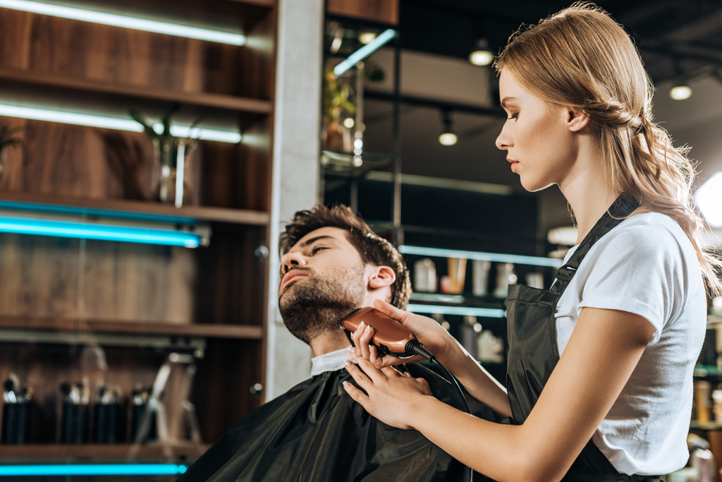 jovem cabeleireiro aparar barba para bonito cliente no salão de beleza
 - Foto, Imagem