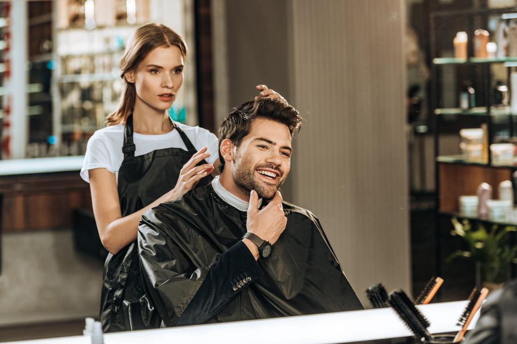 fryzjerka kobiece młody i przystojny człowiek uśmiechający się patrząc w lustro w salonie piękności - Zdjęcie, obraz