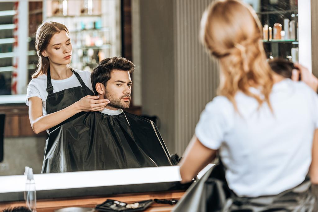 Reflexion im Spiegel des Friseurs, der im Schönheitssalon eine Frisur für eine gutaussehende Kundin macht - Foto, Bild