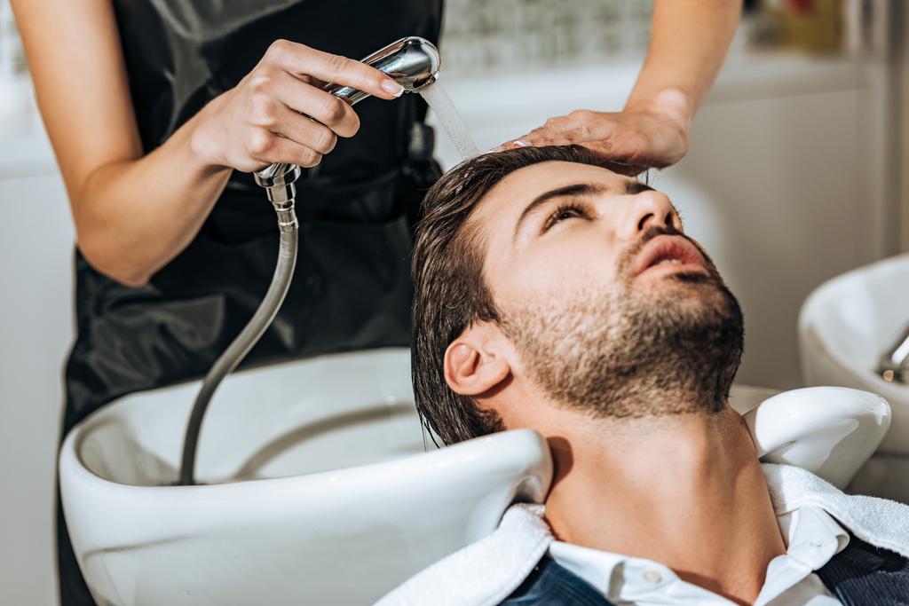 částečný pohled kadeřnice mytí vlasů pohledný mladý muž klientovi v salonu krásy   - Fotografie, Obrázek