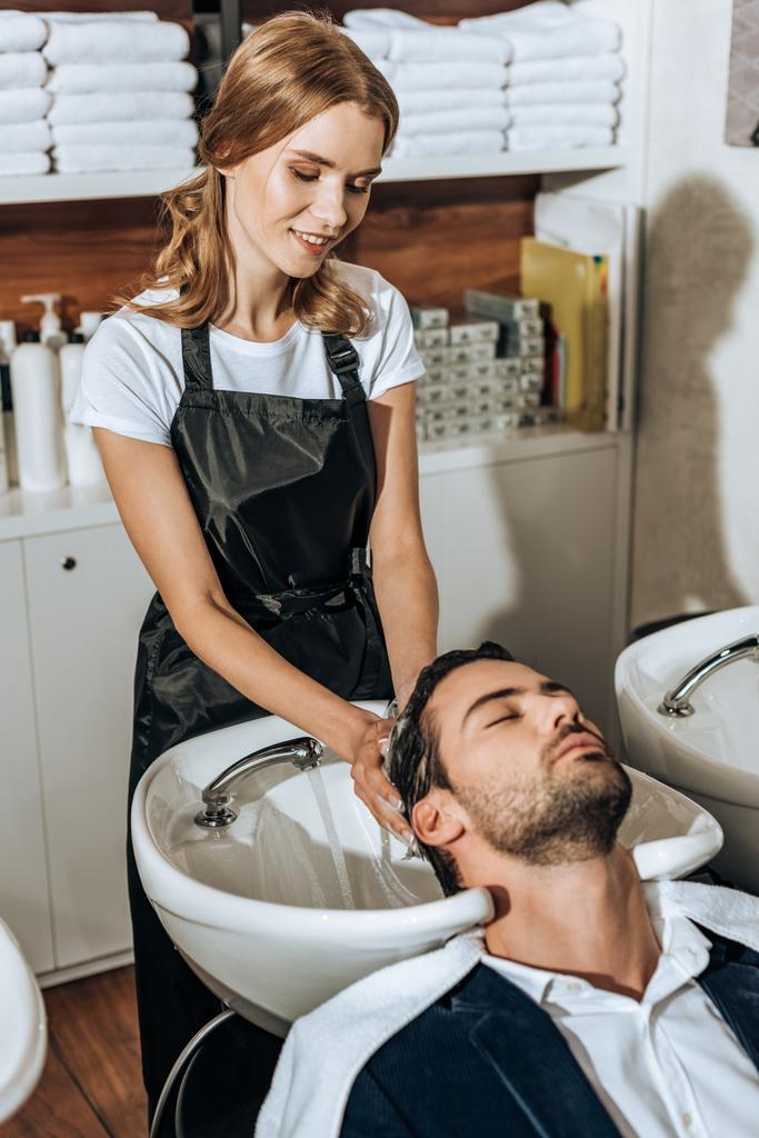 peluquero femenino sonriente lavando el cabello a un joven guapo en el salón de belleza
 - Foto, Imagen