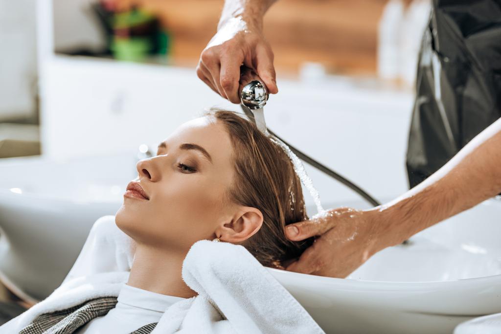 visão parcial do cabelo de lavagem cabeleireiro a mulher jovem atraente no salão de beleza
 - Foto, Imagem