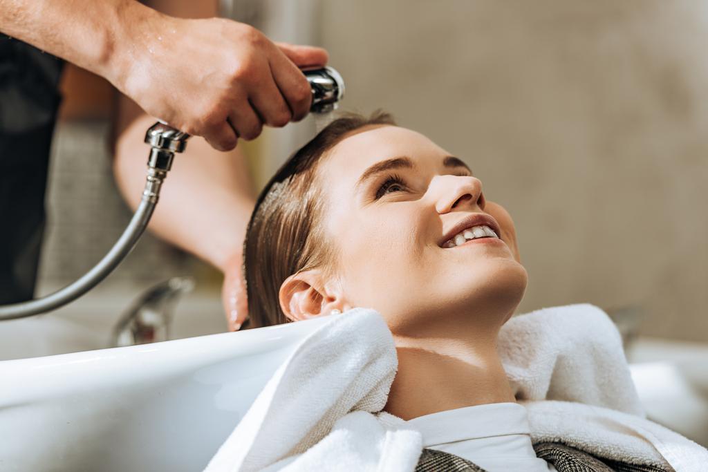 обрезанный снимок парикмахера, моющего волосы привлекательной улыбающейся девушке в салоне красоты
  - Фото, изображение
