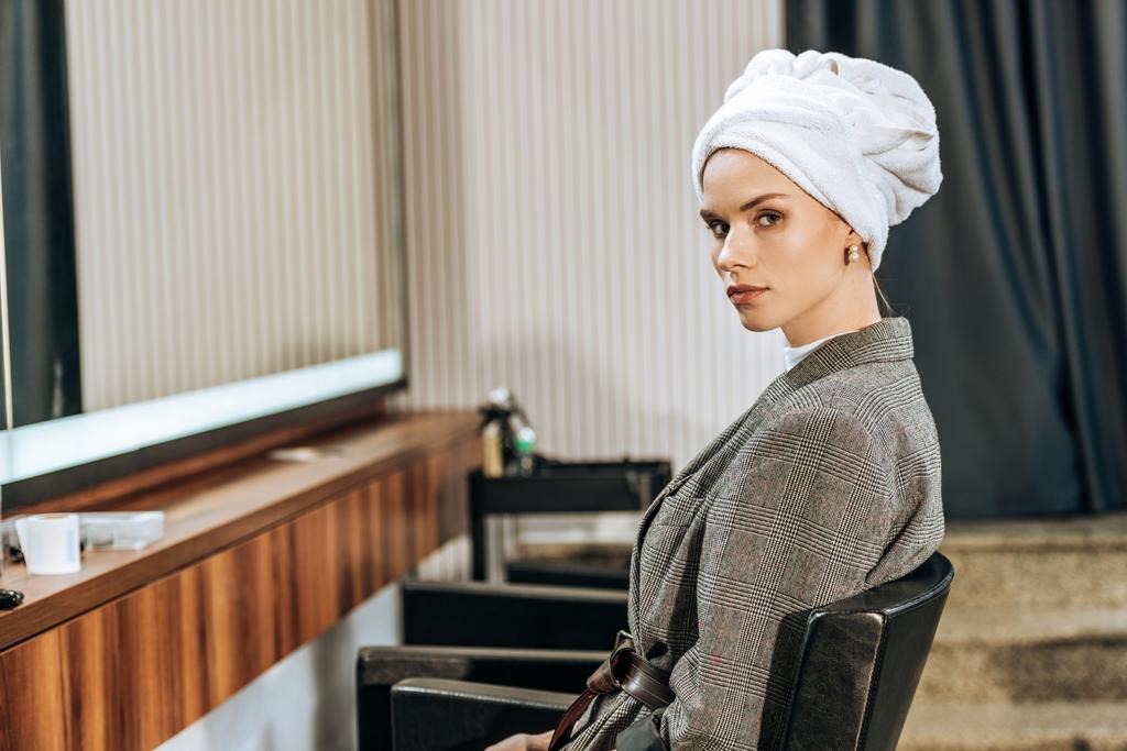 houkutteleva nuori nainen pyyhe pään päällä istuu ja katselee kameraa kauneushoitolassa
 - Valokuva, kuva