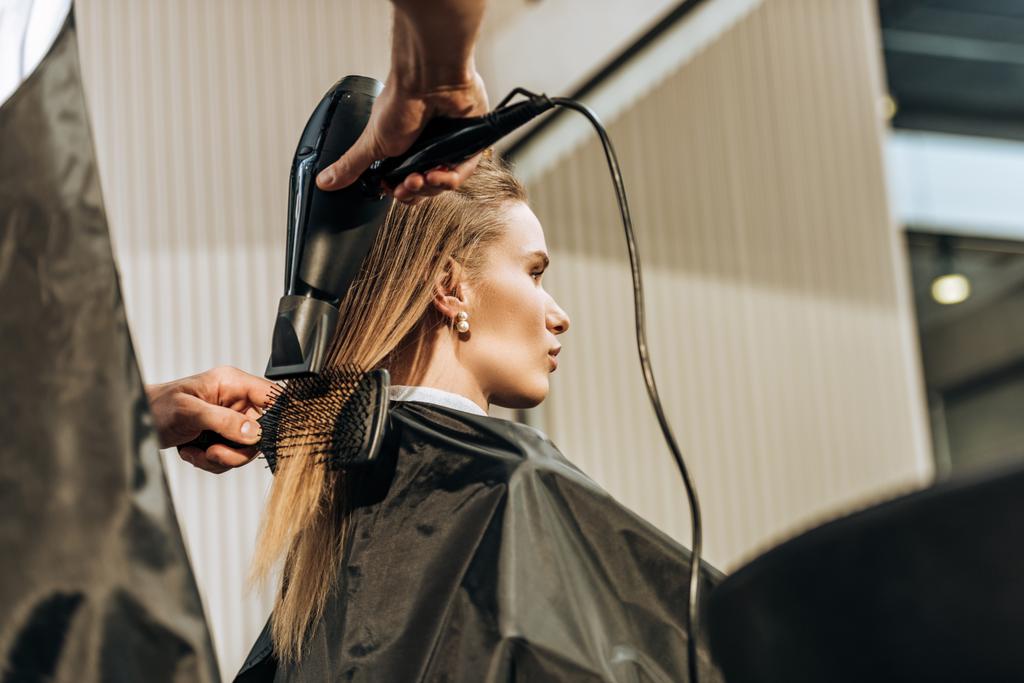 nízký úhel pohled kadeřnice sušení vlasů atraktivní dívka v salonu krásy   - Fotografie, Obrázek