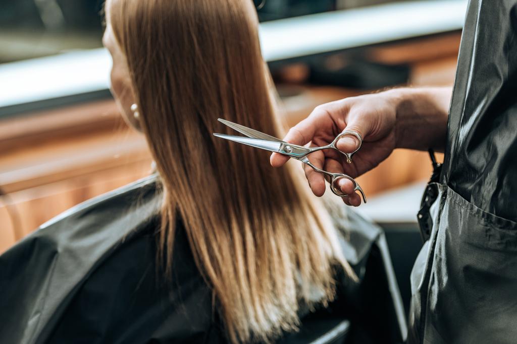 обрізаний знімок перукаря тримає ножиці і молоду жінку, яка відвідує салон краси
 - Фото, зображення
