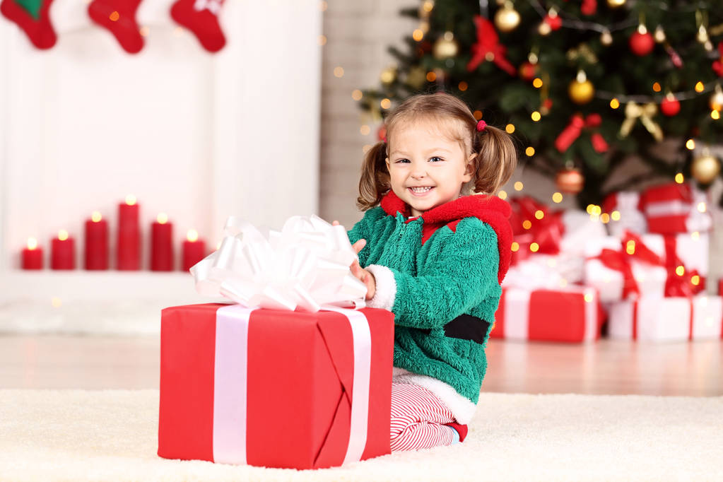 Dziewczynka w kostium z prezent pudełko siedzący choinki w domu - Zdjęcie, obraz