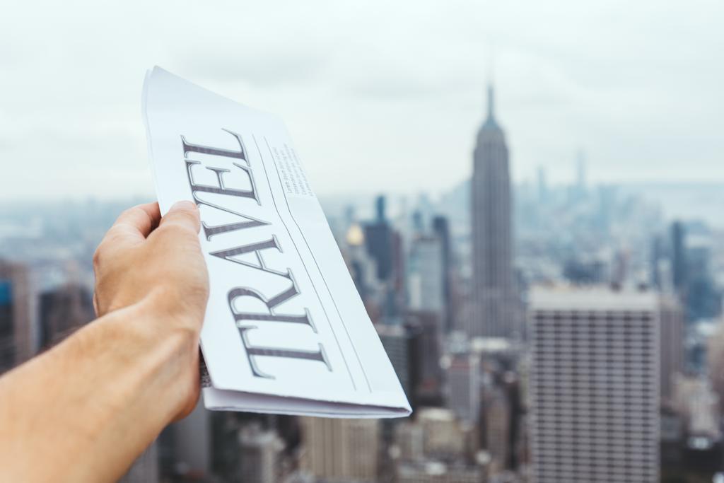 partial view of man holding travel newspaper with blurry new york city view on background - Photo, Image